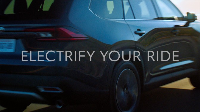 A video still from later in the same add of the vehicle from behind continuing on a road. A super that reads “Electrify Your Ride” is fading out. 