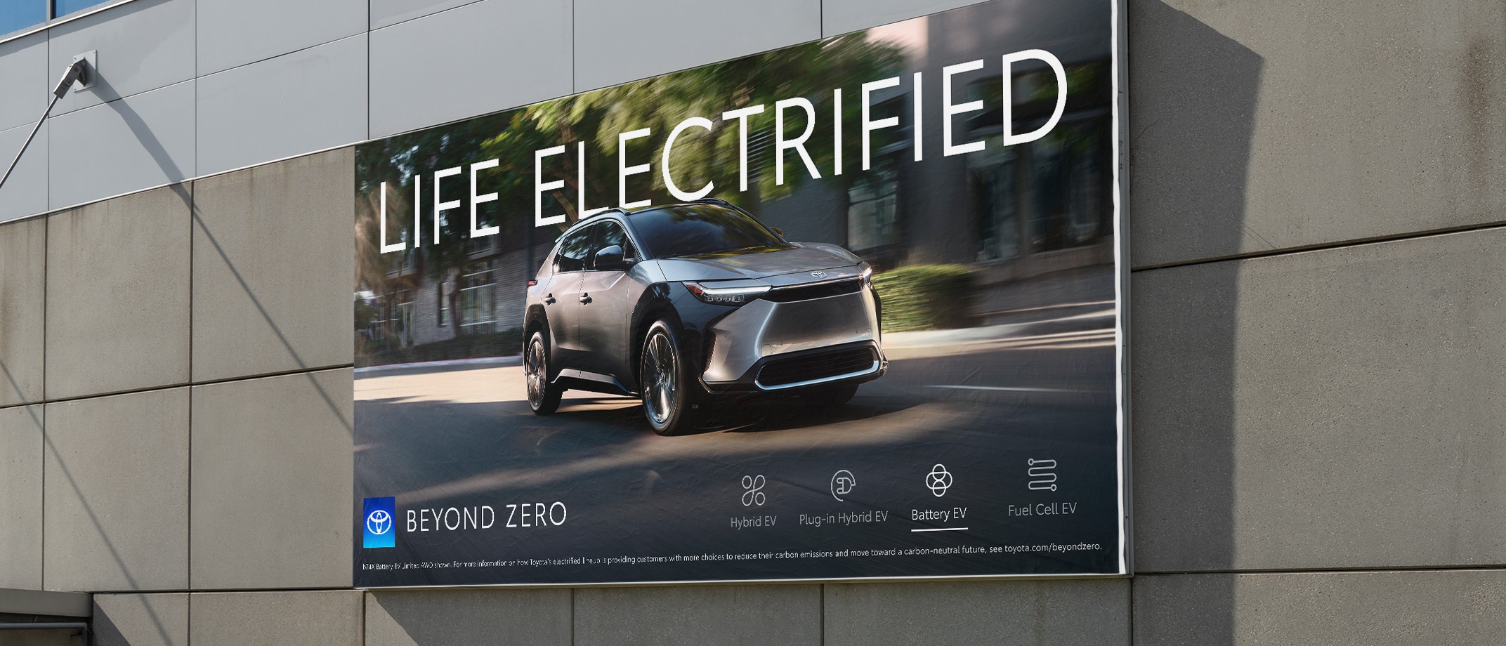 A Toyota out of home ad with the Beyond Zero logo, a Toyota electrified vehicle driving down a city street and a headline that reads Life Electrified.