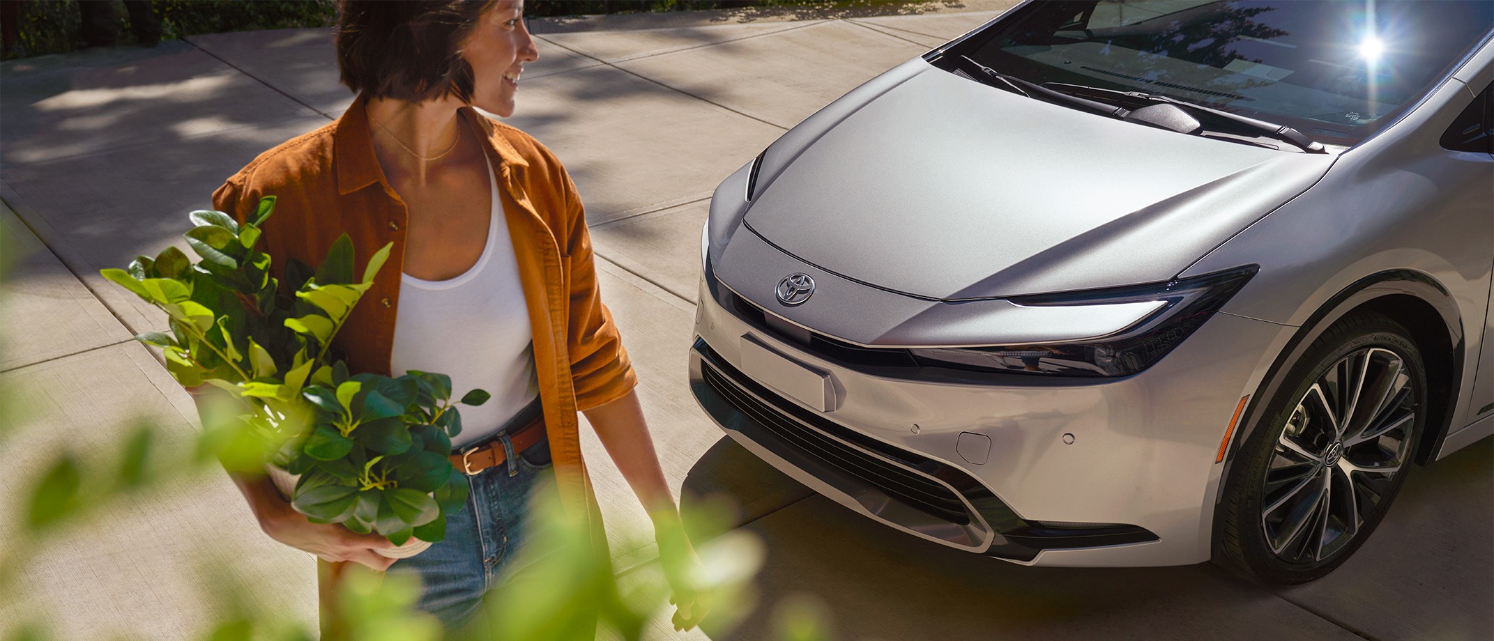 Image treated with Toyota Color Profile showing a sunny day and a woman holding garden plants walking away from her electrified vehicle.