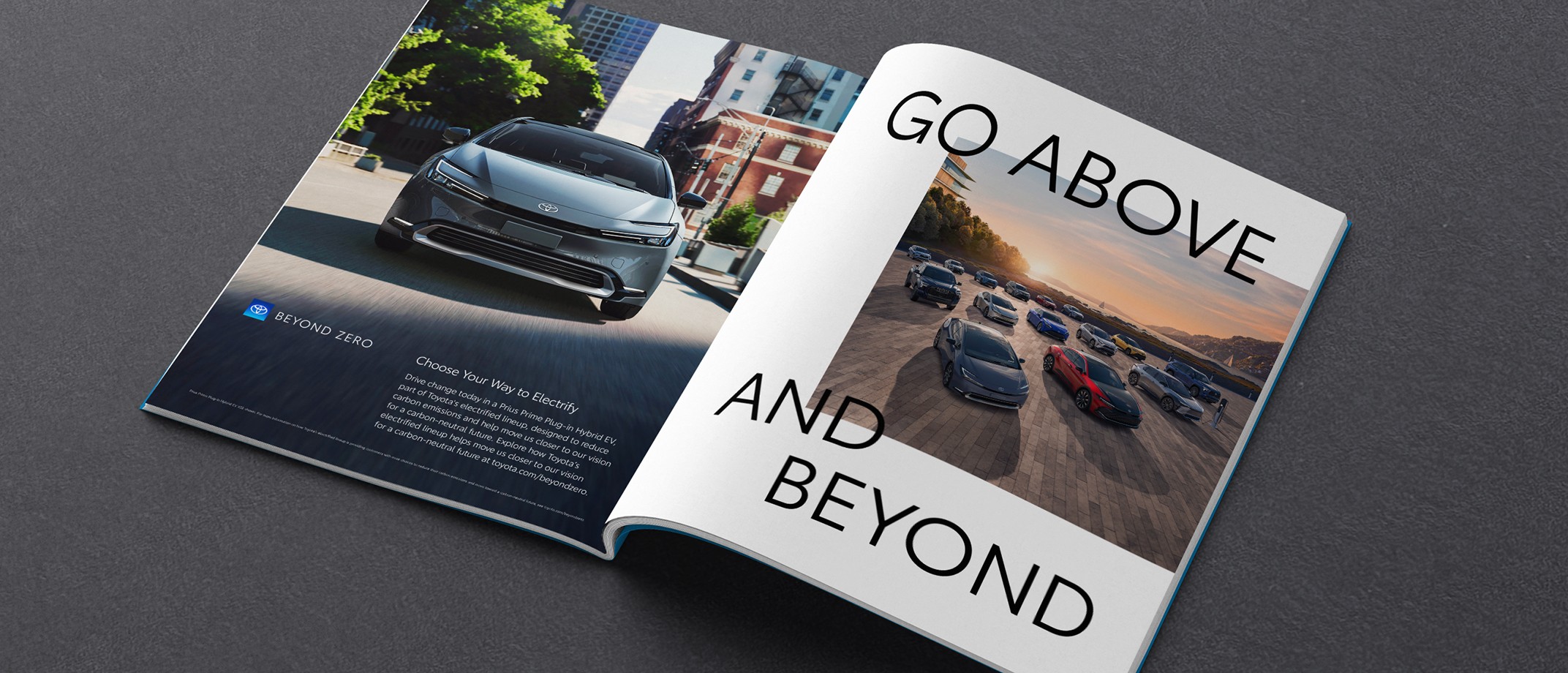 An open magazine against a dark grey background. The open pages of the magazine display a Toyota ad featuring the lineup of Electrified Vehicles, body text, the Beyond Zero logo and a headline that reads “Go Above and Beyond.”