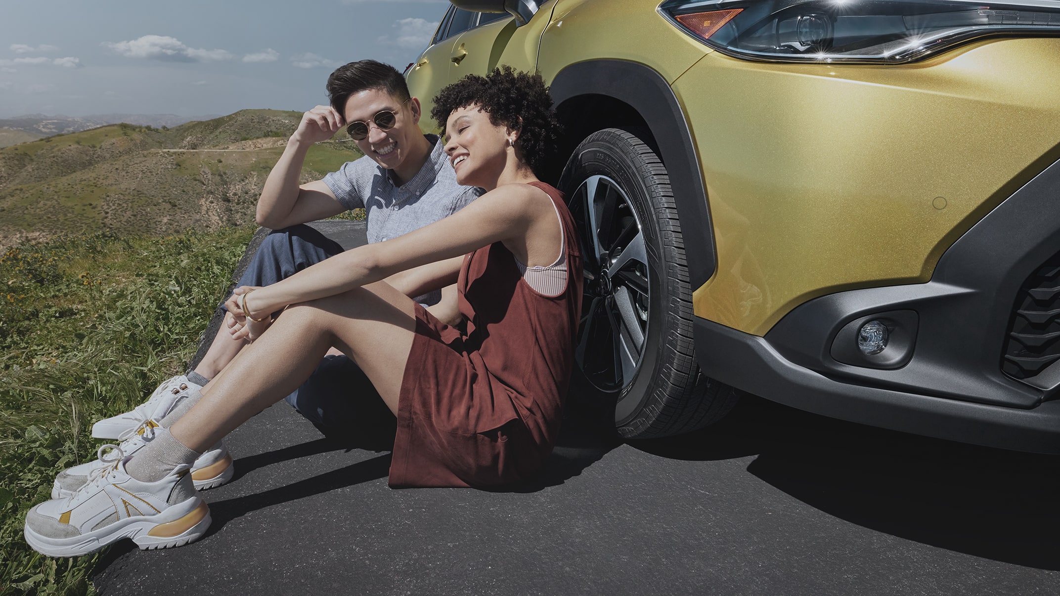 A couple sits next to their Corolla Cross, overlooking the mountains on a sunny day. A slider divides the image in half, showing what it looks like when color profile is added to the image.