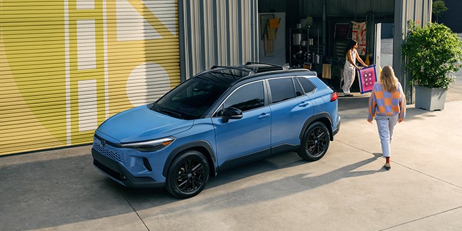 Blue car parked in front of a yellow wall with woman walking outside