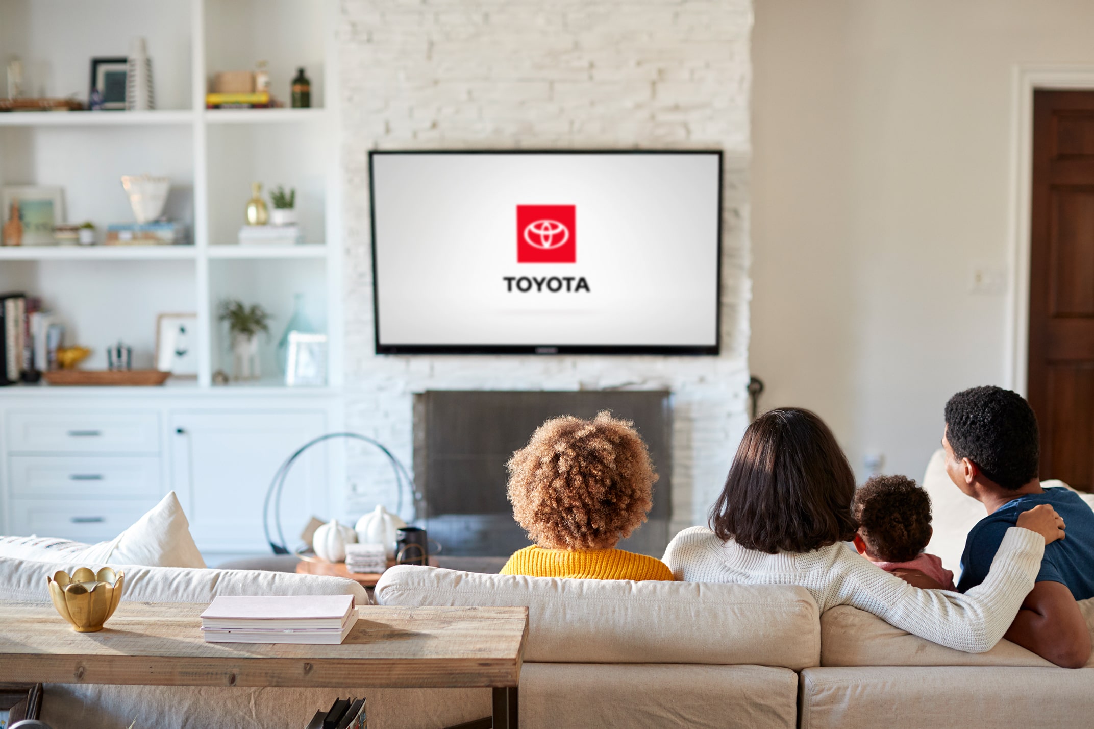 A family sitting together on their couch is watching TV. The Toyota end tag is displayed on the TV screen.