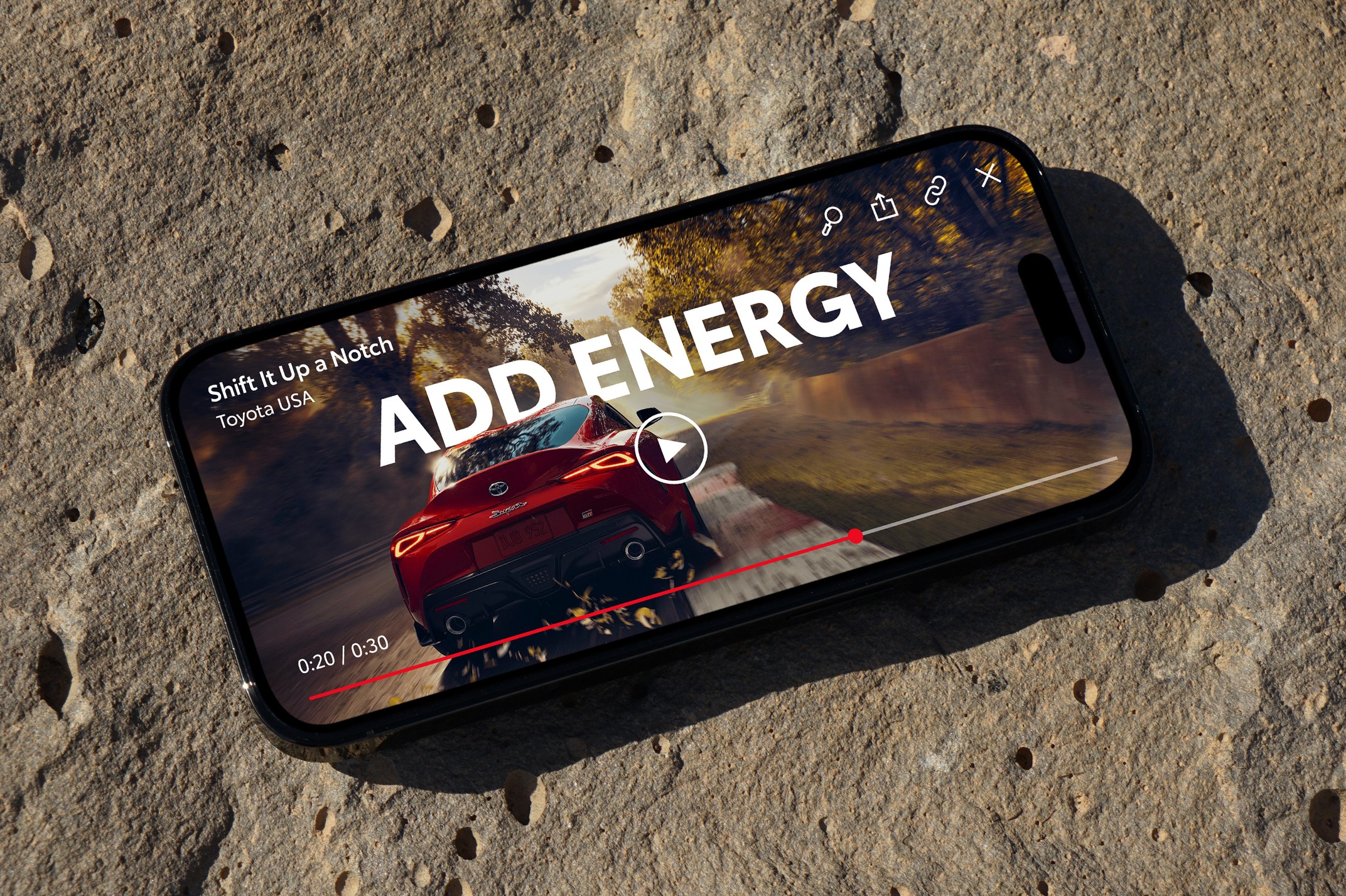 An iPhone sitting on top of a Mac keyboard displays a paused video of Supra footage with a super reading “ADD ENERGY.”