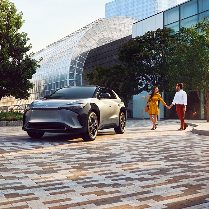 An image of a city scene with a couple walking towards a parked electrified vehicle.