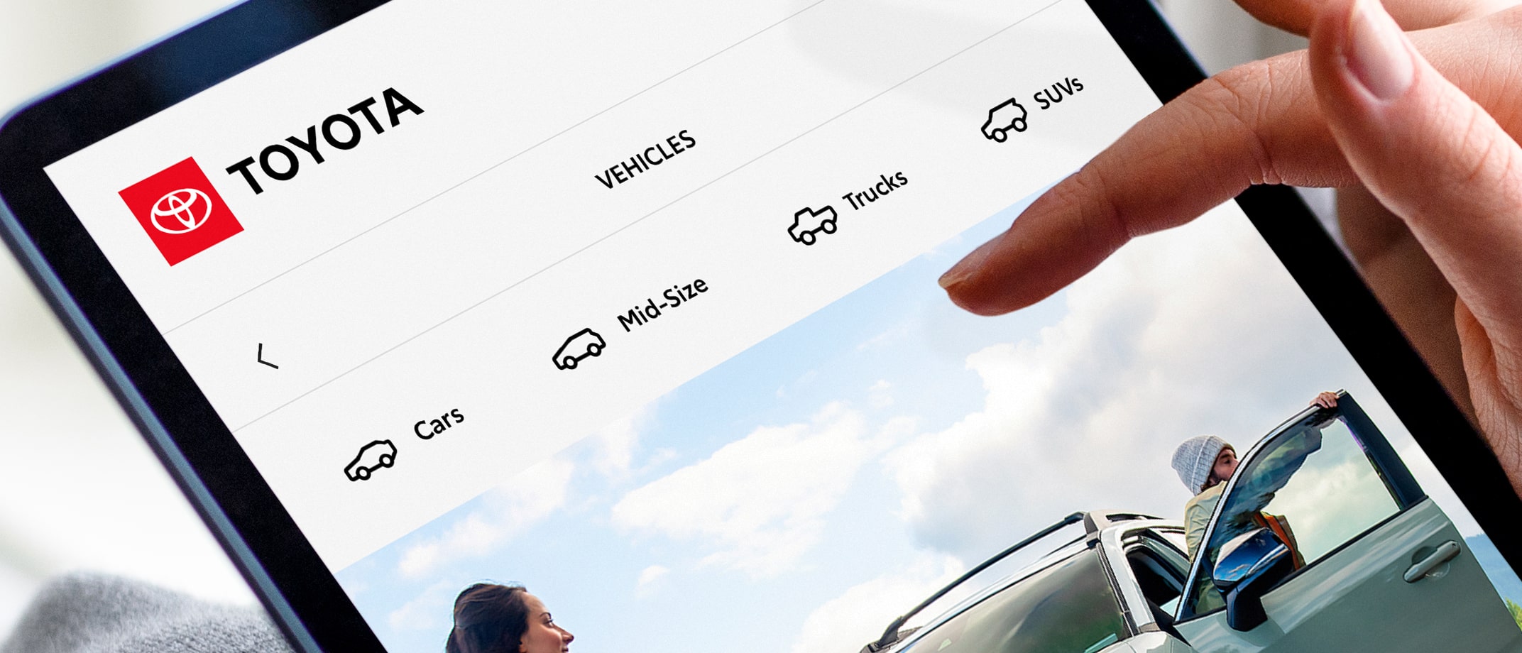 A hand hovers above a tablet screen showing a Toyota webpage with different vehicle icons for “Cars,” “Mid-Size,” “Trucks” and “SUVs.”
