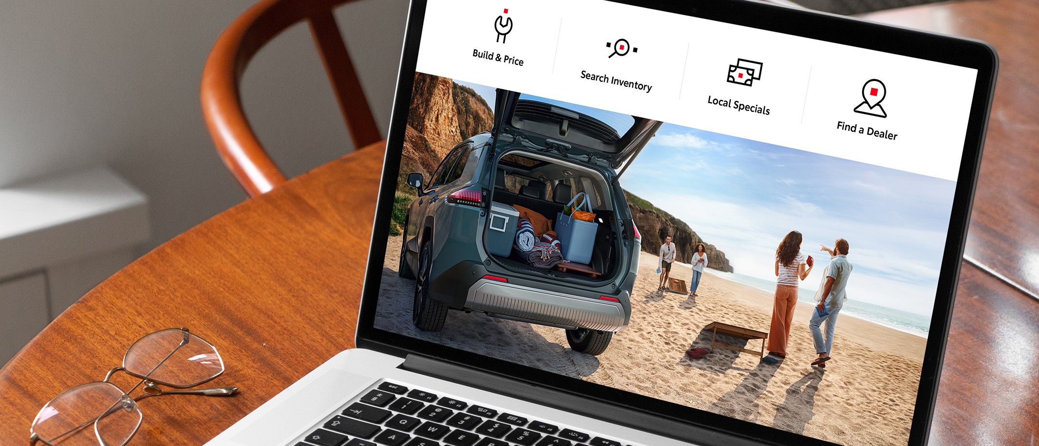 A laptop on a white desk. On the screen is a Toyota website with large icons in the top menu for “Build & Price,” “Search Inventory,” “Local Specials “ and “Find a Dealer.”