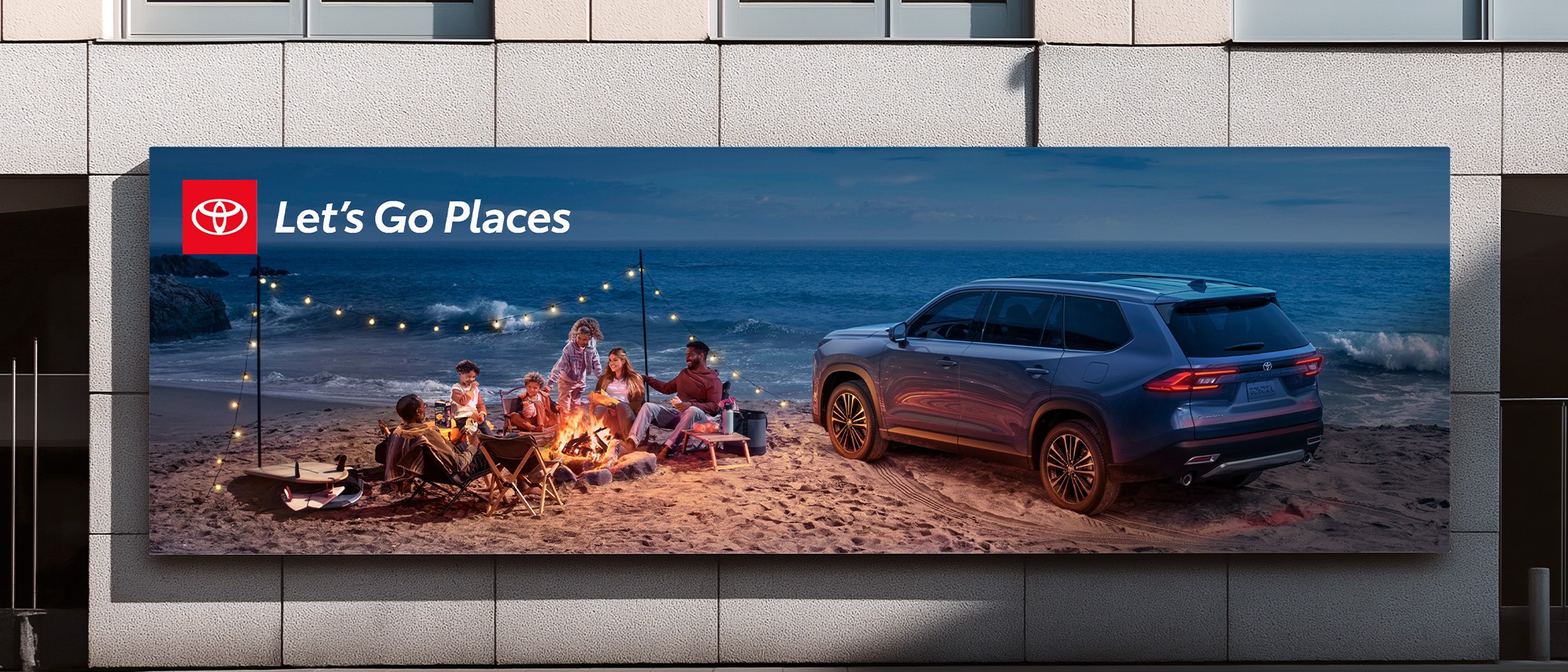 An ad with the Let’s Go Places logo. In the image, next to the ocean, a family sits by a bonfire on the sand.