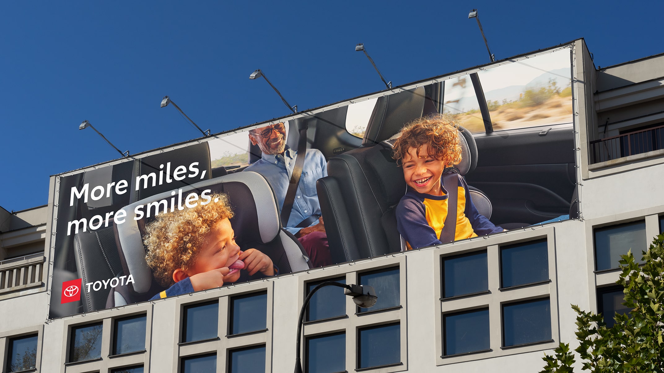 An out-of-home billboard with the Toyota logo shows a family inside their Grand Highlander. The headline reads “More miles, more smiles.”