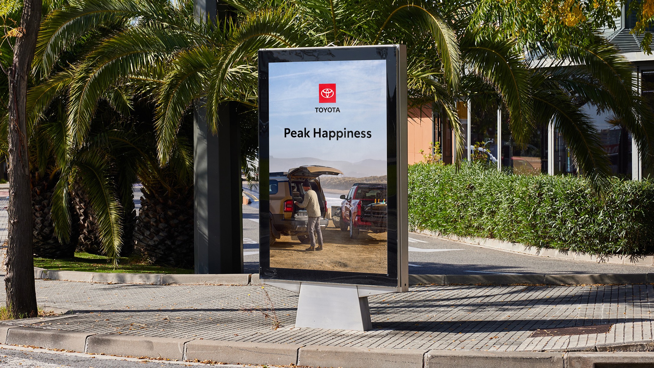 An out-of-home billboard with the Toyota logo shows two different Toyota models in front of the ocean with the tagline “Peak Happiness”.