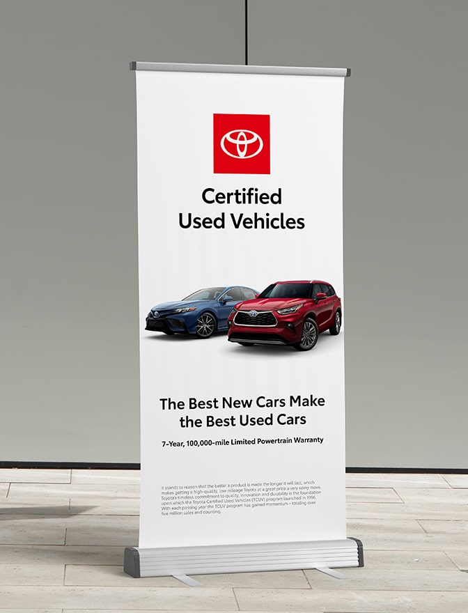 A banner stand displays a sub-brand ad inside a building. It has the Certified Used Vehicles logo with an image of two vehicles and a headline.