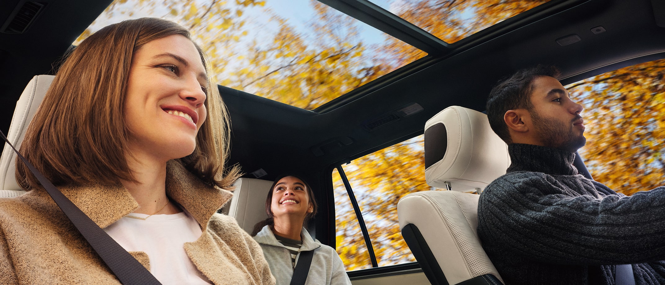 A couple on a drive with fall foliage; their daughter in the background looks up through the moonroof to take it all in.