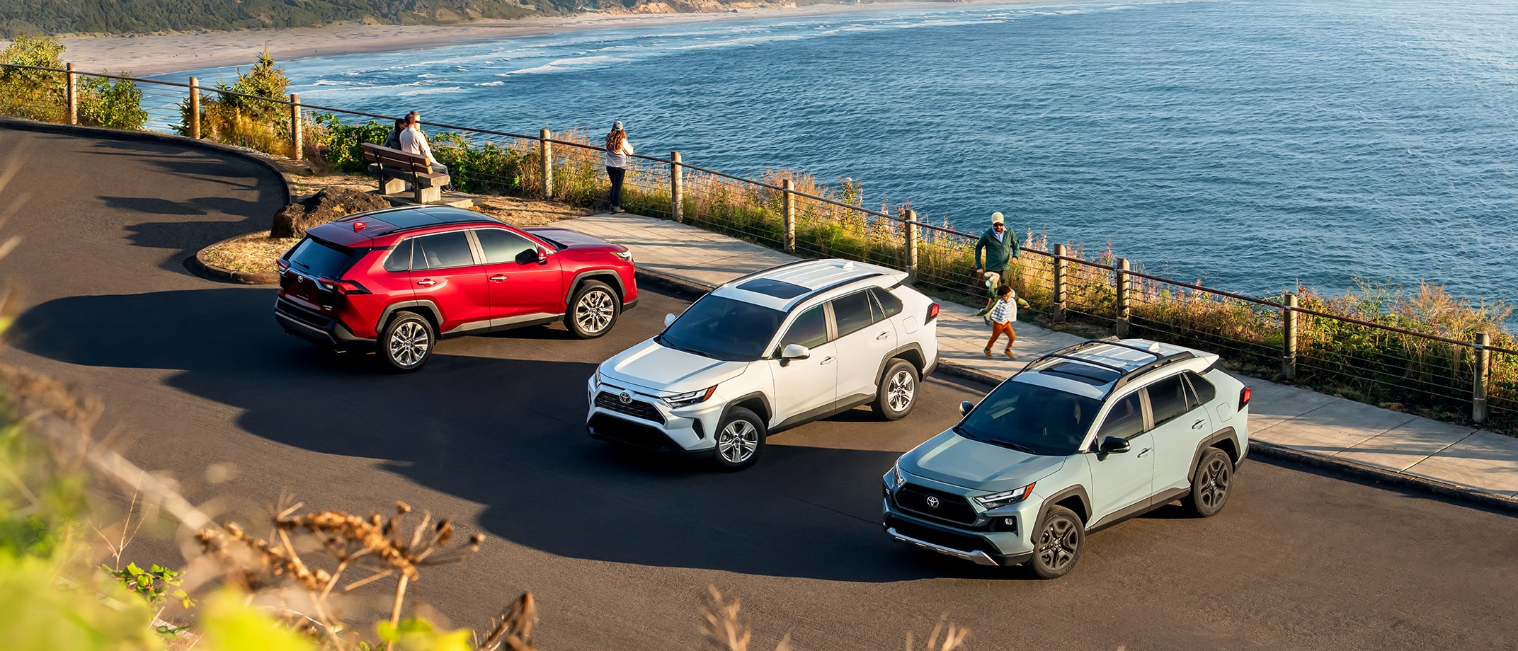Three Toyota vehicles in the parking lot next to an oceanside viewpoint.