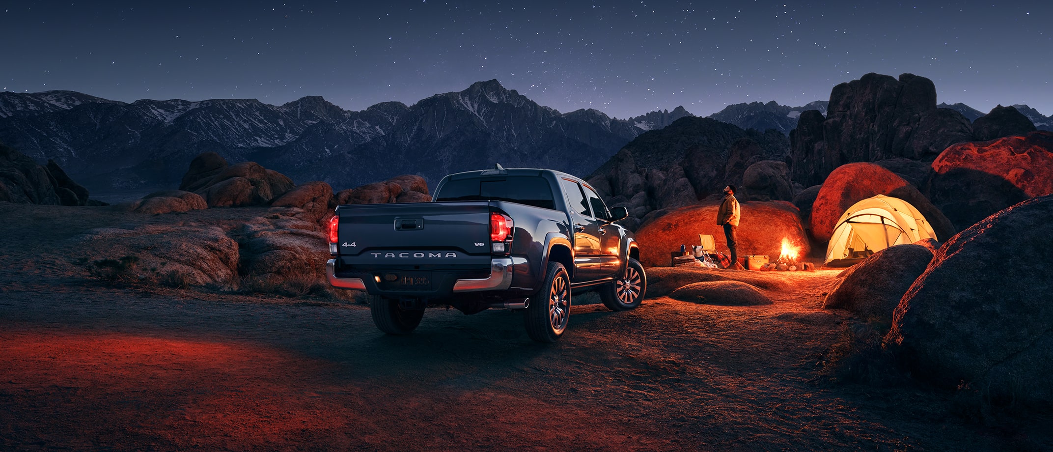 The Toyota Tundra is parked among boulders and mountains, right next to a campsite with a tent and campfire.