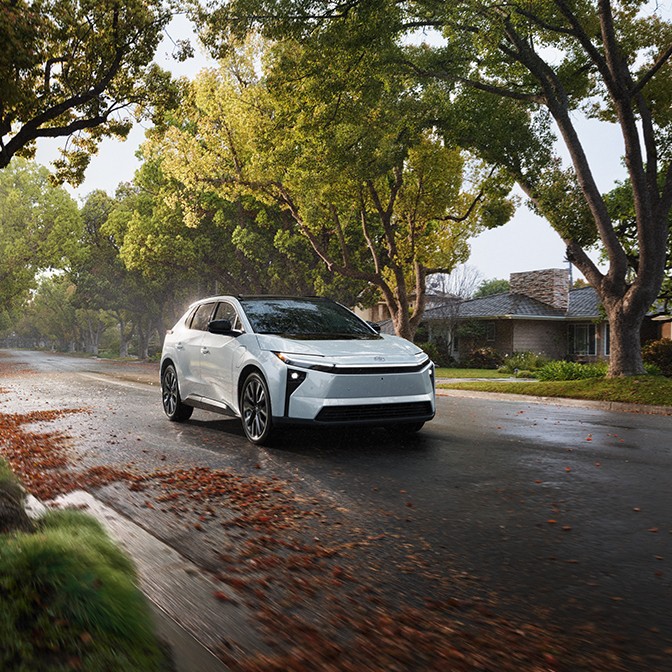 A car driving down a road lined with trees and leaves.