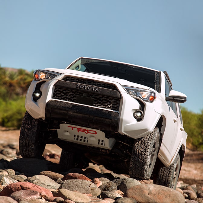 The front grille of a white truck on rocky terrain.