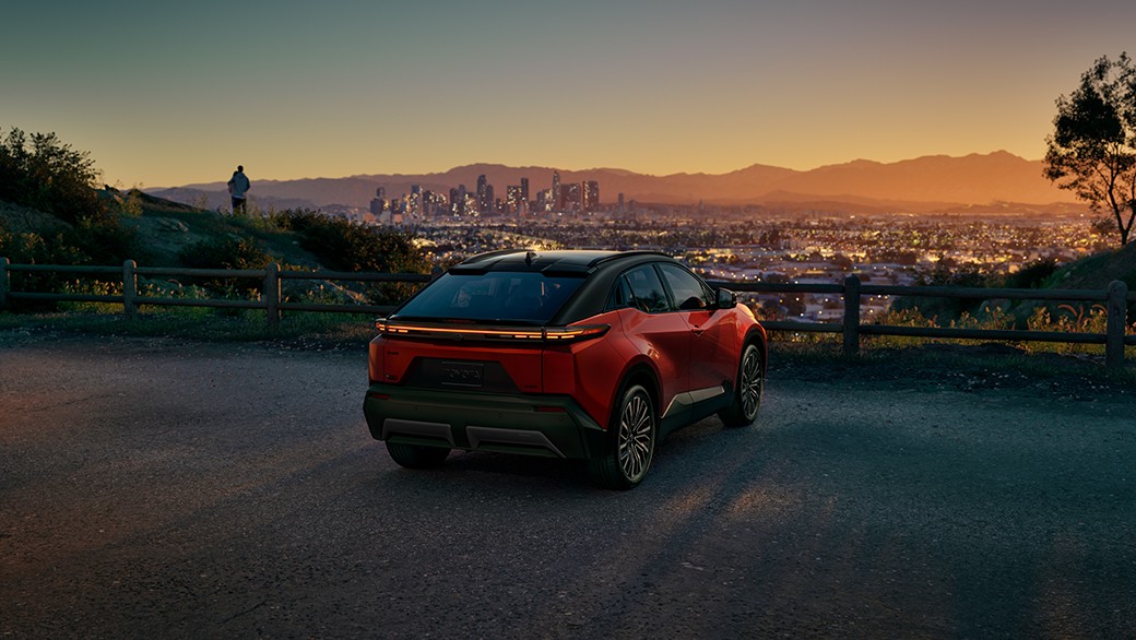 A red car on a road with a city in the background.