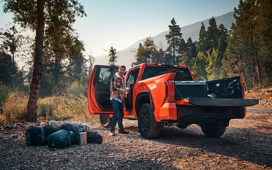 A man unloads gear from a Tundra TRD Pro, with woods and mountains in the background.