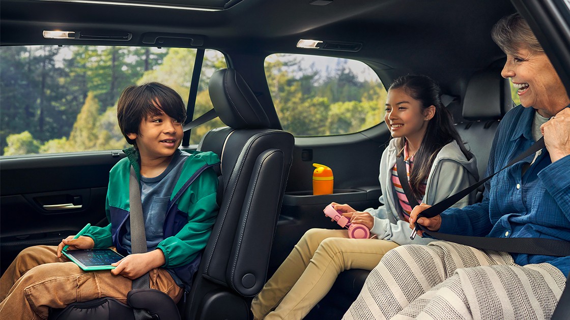 Little boy sitting in the front, with little girl and woman sitting in the back, all smiling together in the car.