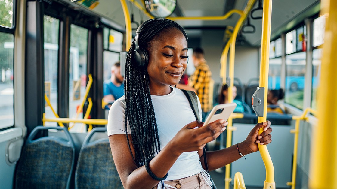 A girl on a bus with headphones on looking at her phone.