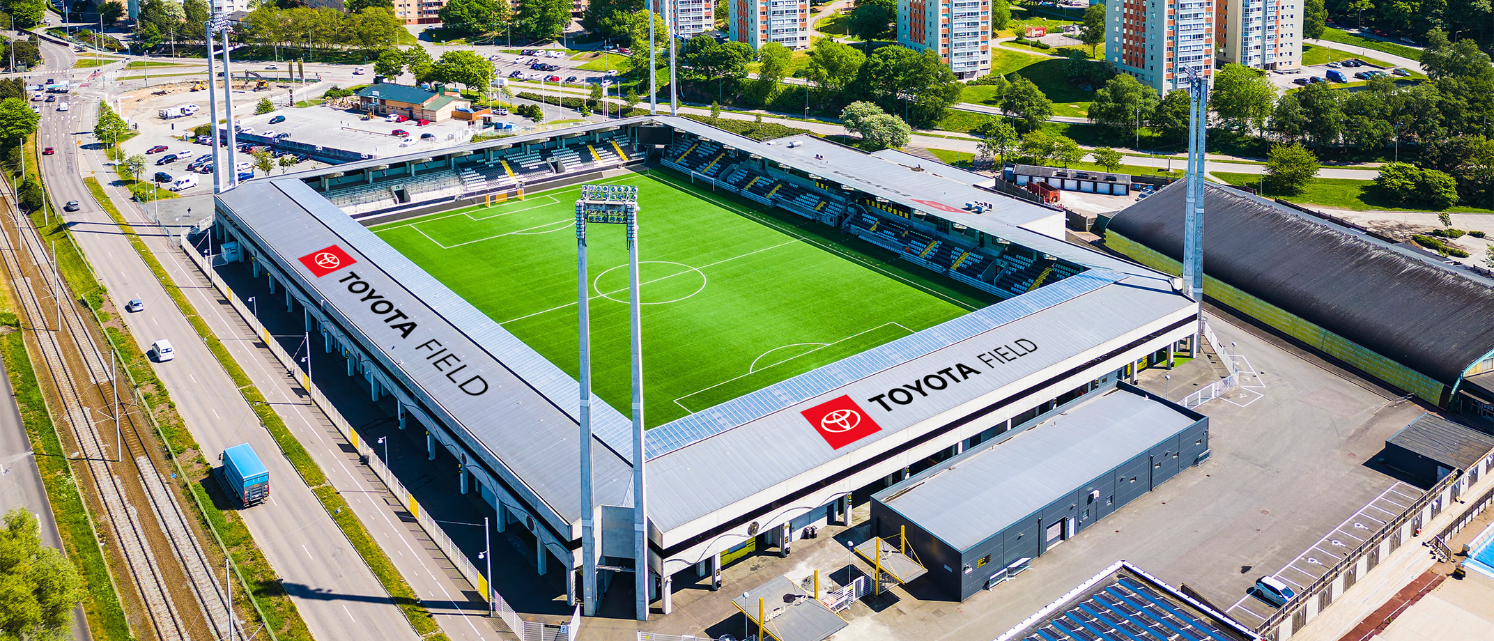 A range of Toyota Type signage examples including a soccer field with signage on the sides of the building, wall signage in a club bar, a signage banner hanging above stands in a  stadium, signage on the entry doors of a large building.