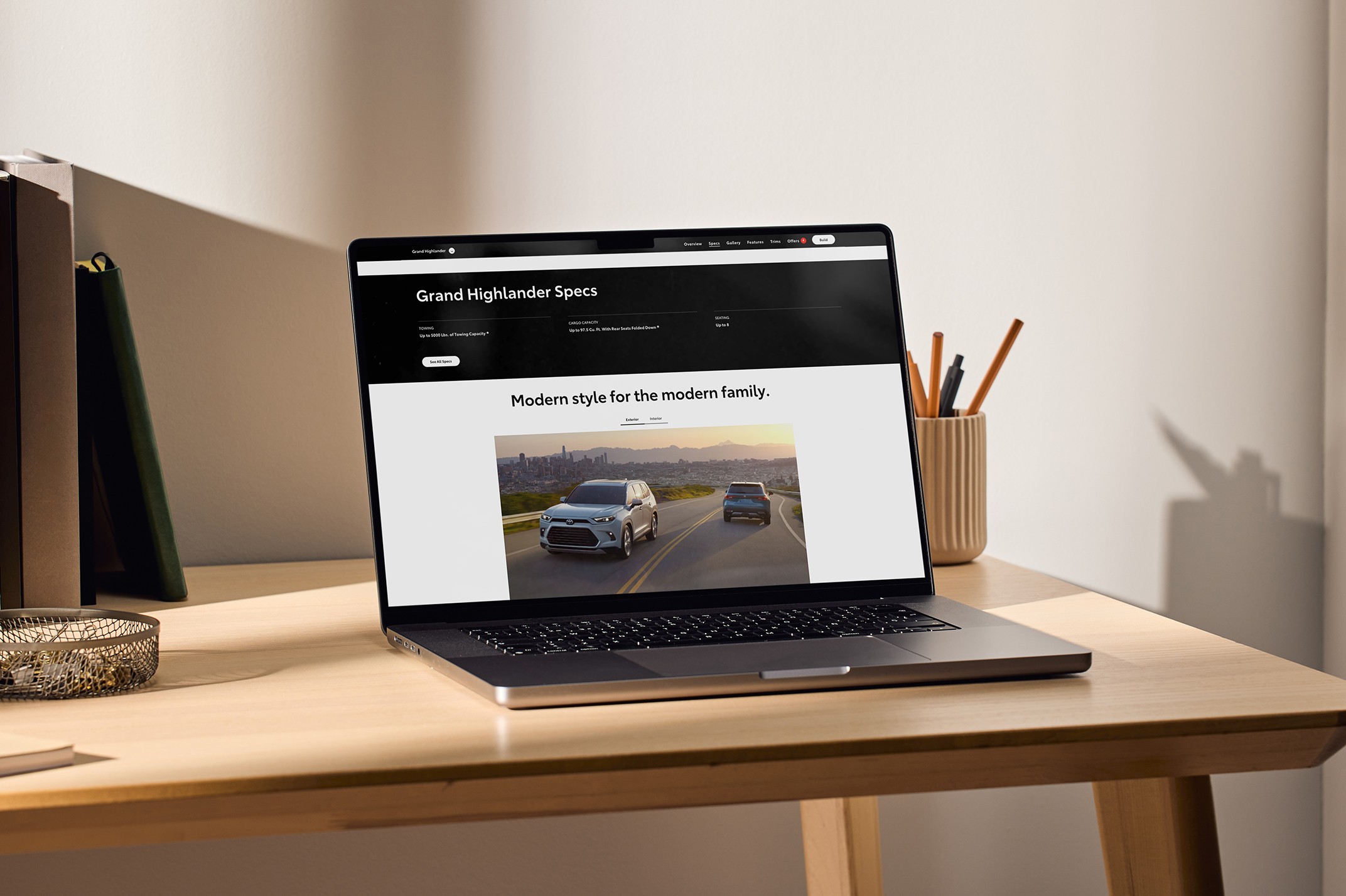 A laptop sits on a desk. The laptop screen displays a Toyota vehicle landing page.