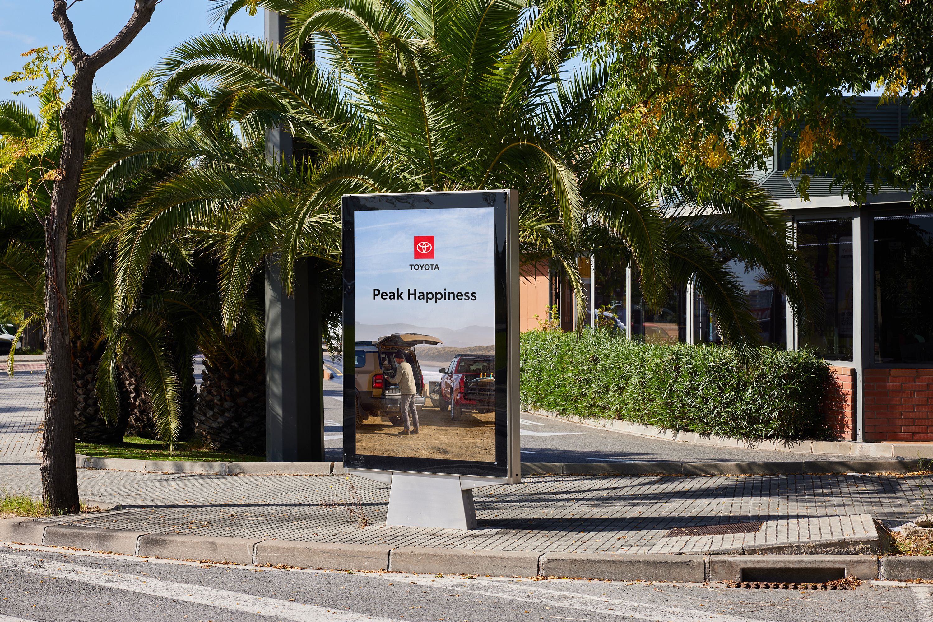 A digital out-of-home sign in a park displays an add with the Toyota logo, headline and two Toyota trucks atop a mountain.