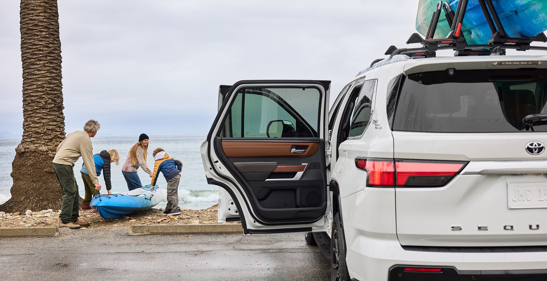 White Sequoia with doors open in front of the ocean with family carrying kayak down to the beach.
