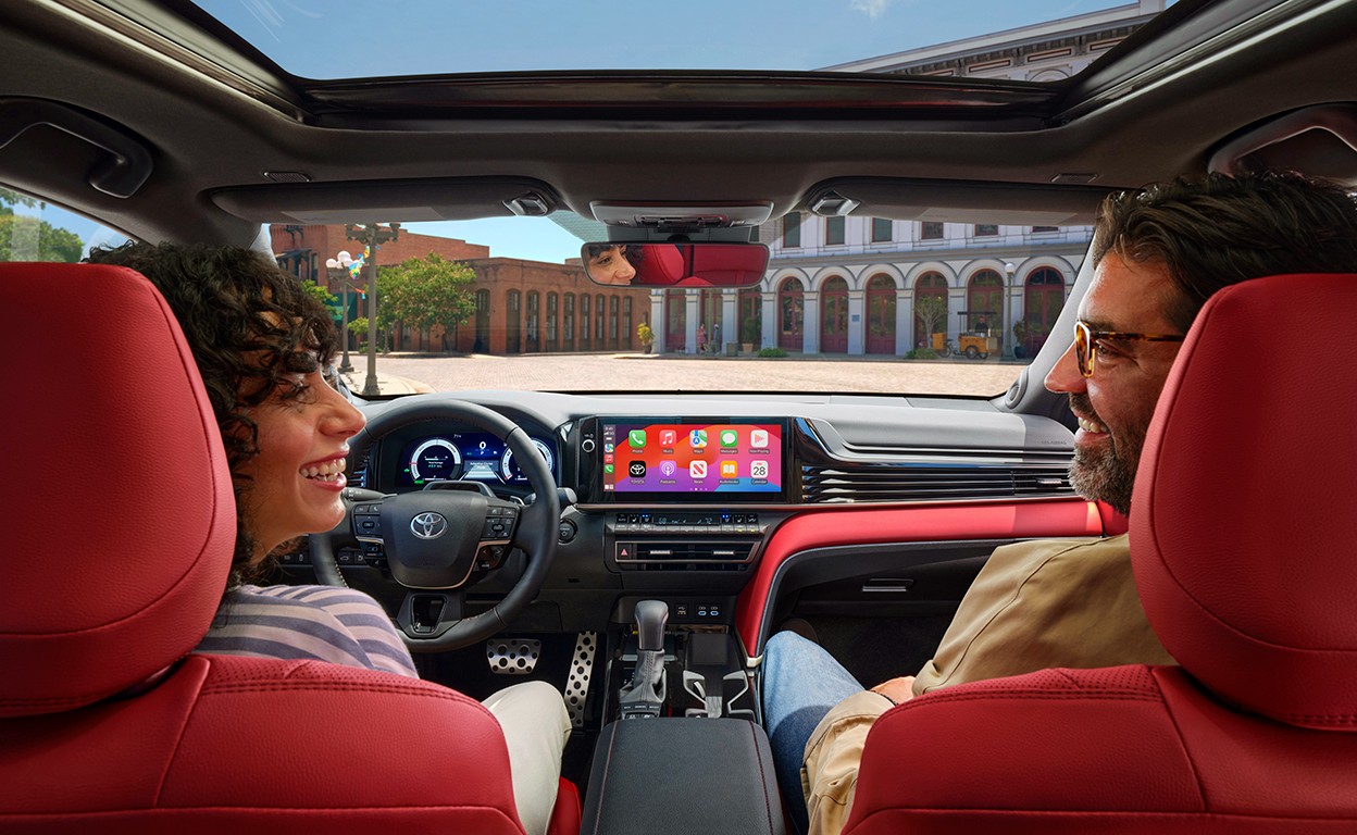 A couple smiles at each other inside a vehicle with red seats and a moonroof.