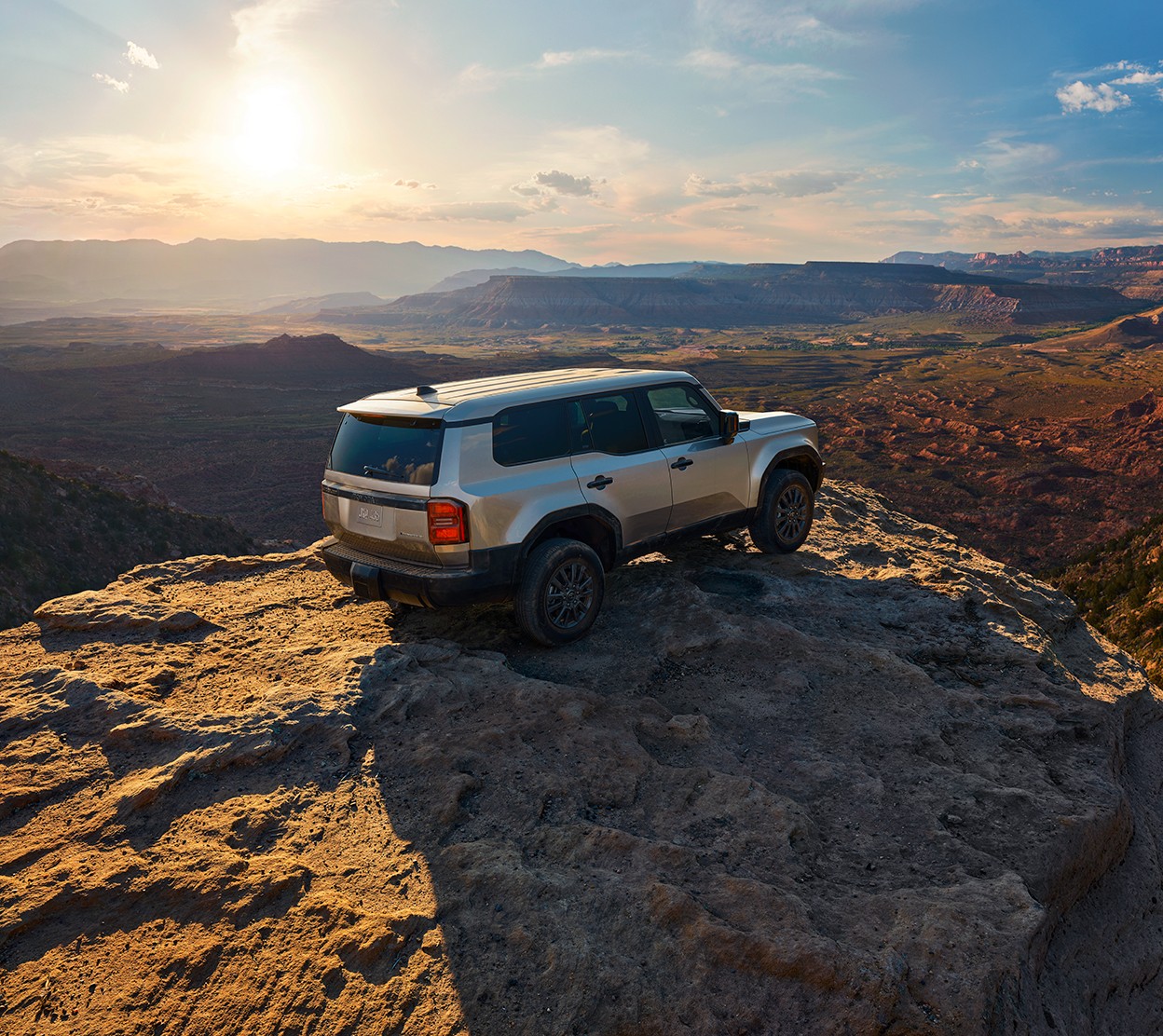A Toyota truck is parked atop a rocky hill with a sunny mountain overlook in the background.