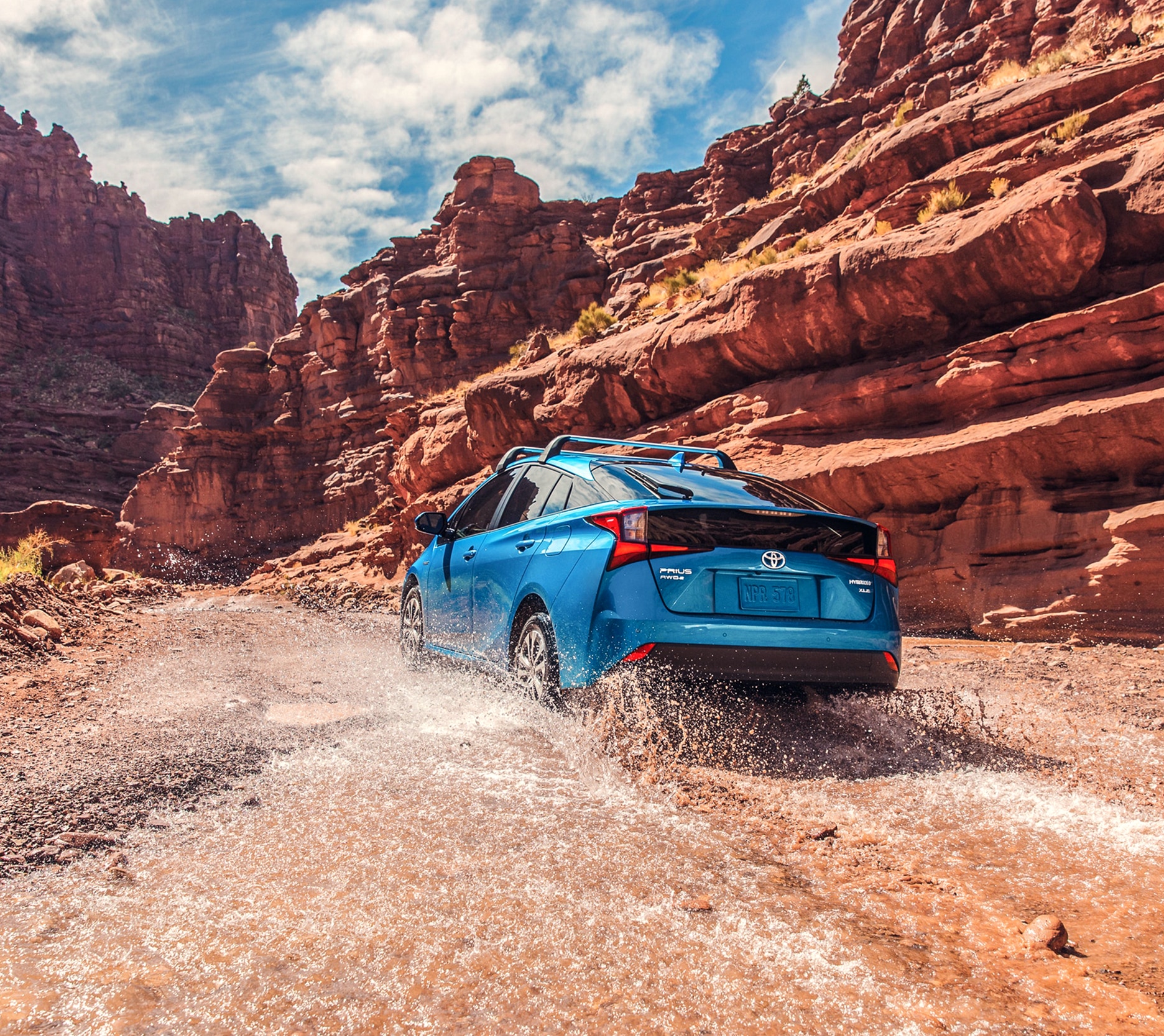 Rearview of a Toyota Prius driving through a stream next to rock formations.