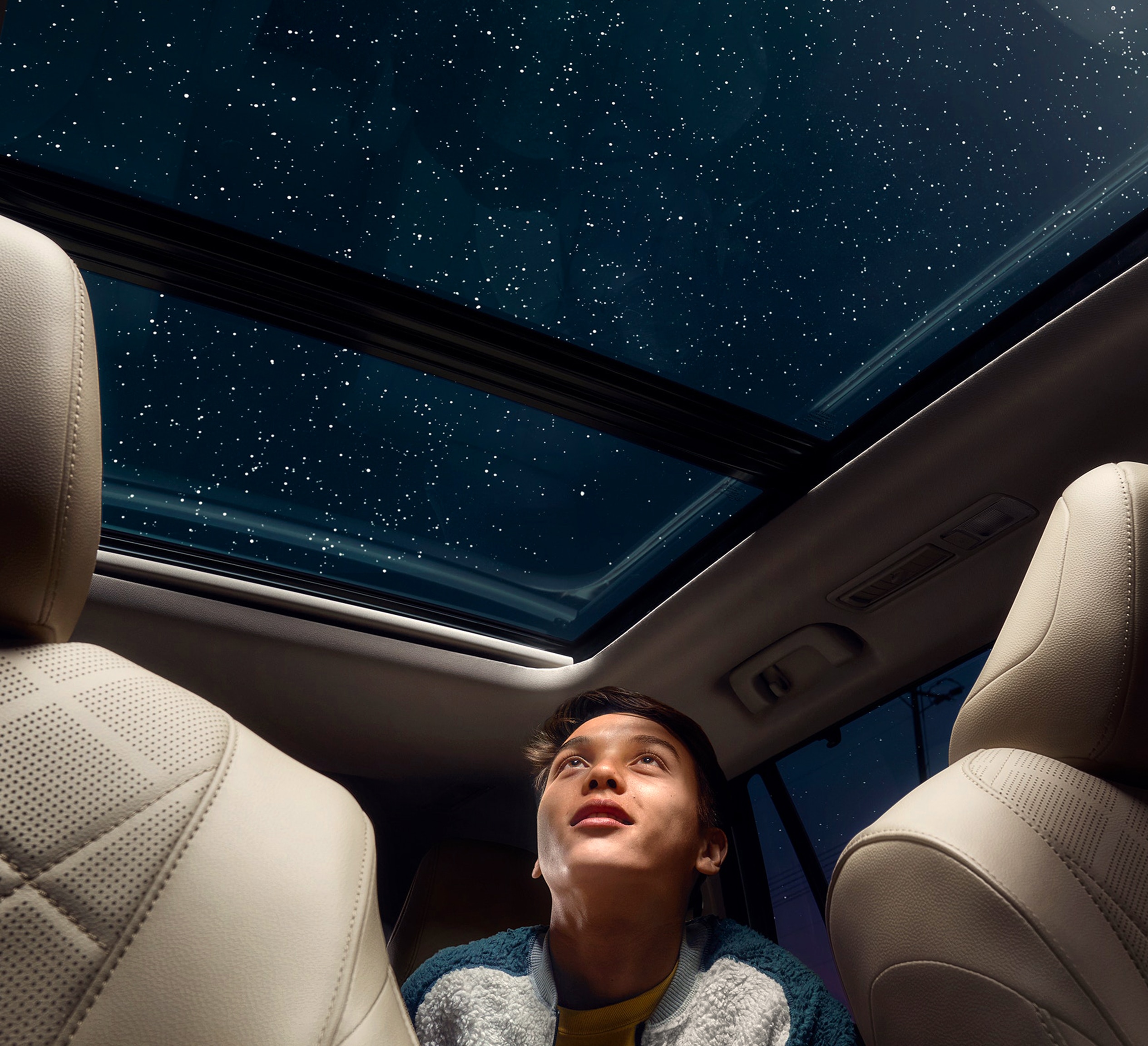 Boy looking up through the moonroof of a Toyota Highlander to a night time sky.