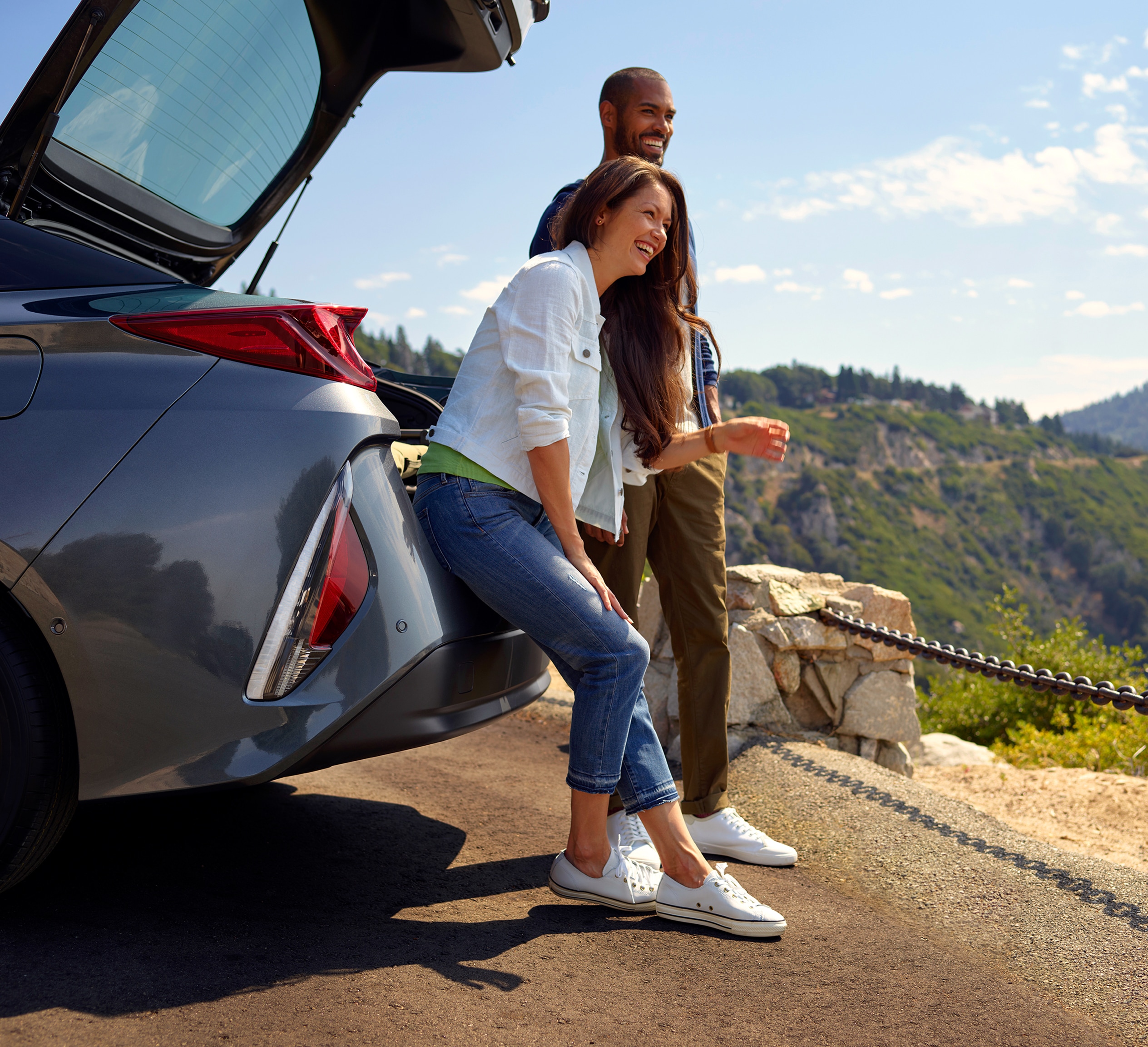 Woman and man standing behind a Toyota Prius Prime with hatch open on a scenic overlook.