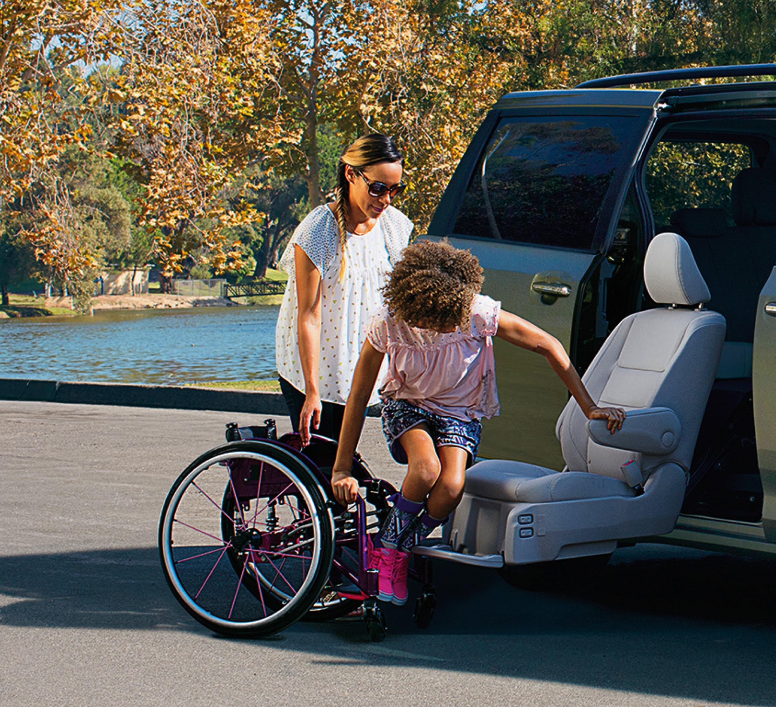 Woman helping girl move from wheelchair to Toyota Sienna Auto Access Mobility Seat.